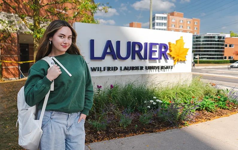 Female student standing beside Wilfrid Laurier University sign